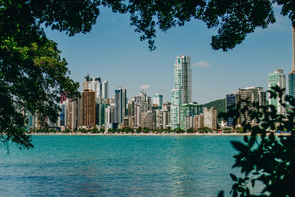 A vibrant city skyline with skyscrapers by a turquoise seafront framed by lush greenery.