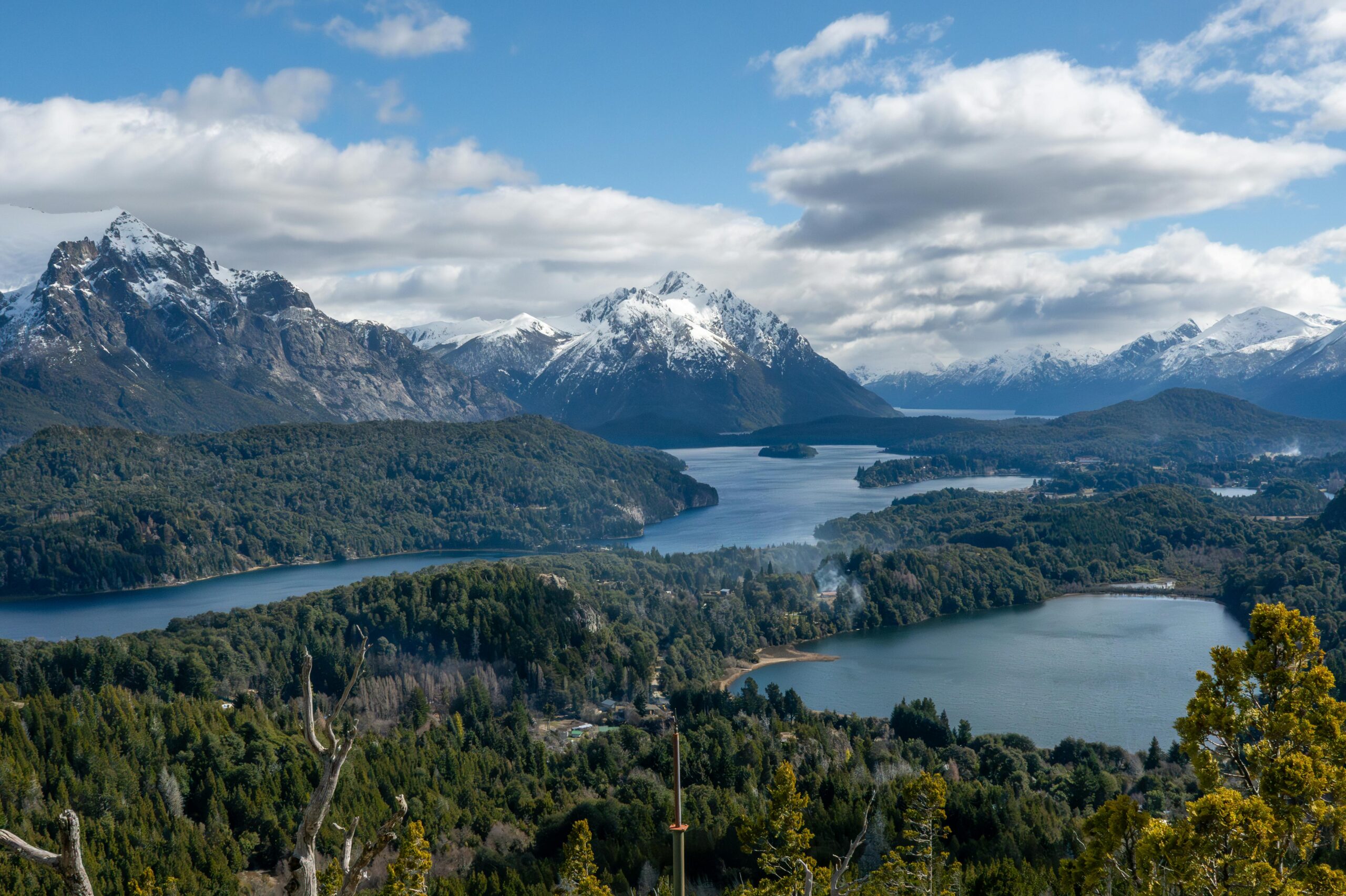 Panoramic landscape of snowy mountains and lakes in Bariloche, Argentina, under a clouded sky.